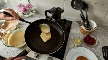 Ev mutfağında yemek pişirirken tavaya hamur döken bir kızın kısmi üst görüntüsü. Ev hayatı kavramı. Sağlıklı beslenme fikri. Modern daire. Gündüz