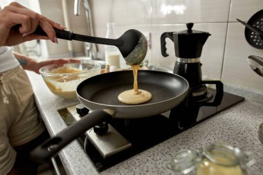 Ev mutfağında yemek pişirirken tavaya mangır döken bir kızın kısmi görüntüsü. Ev hayatı kavramı. Sağlıklı beslenme fikri. Modern daire. Gündüz
