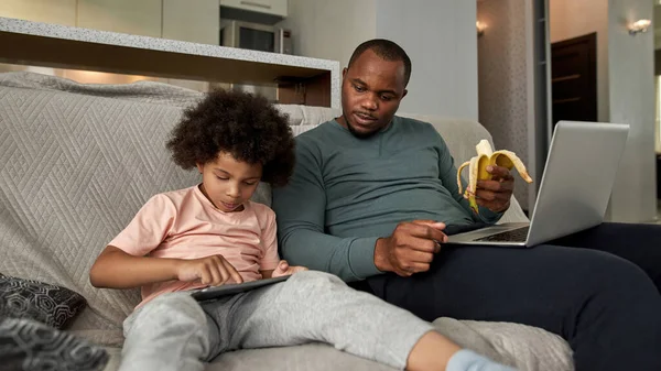 Pai Com Laptop Banana Olhando Para Pequeno Filho Usando Tablet — Fotografia de Stock