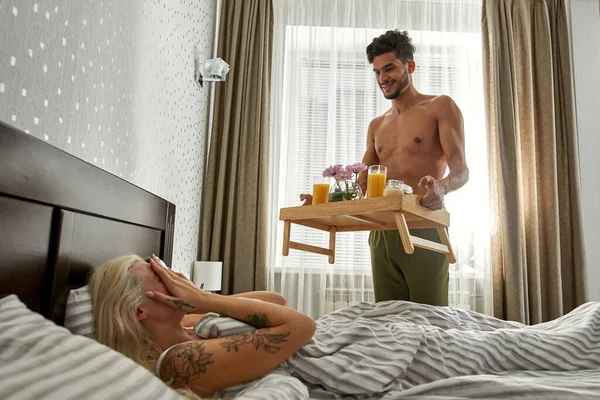 中东男人带着惊喜的早餐放在木制盘子里 让金发碧眼的女朋友蒙面躺在床上 年轻夫妇享受在一起的时光 浪漫的关系 家庭生活方式 — 图库照片
