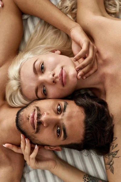 照片上的年轻漂亮的多民族夫妇躺在床上 看着镜头在床上 有纹身的白人女孩和相互接触的中东男人家庭生活方式 隐秘症 — 图库照片