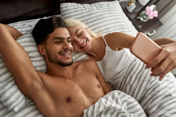 즐거운 침대에서 스마트폰으로 셀카를 있어요 여자와 남자가 쉬면서 시간을 보내고 — 스톡 사진