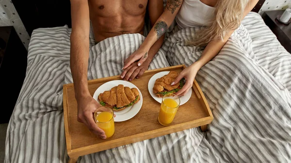 夫妻在家吃早餐 三明治和果汁的部分头像 有纹身的女孩牵着男朋友的手 家庭生活方式 在家里休息吧隐秘和关系 — 图库照片