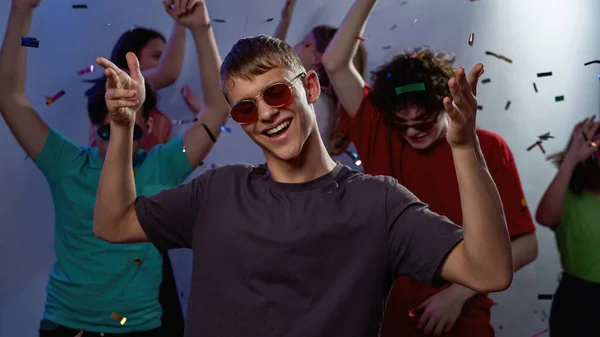 楽しい白人の十代の若者は 眼鏡をかけて踊り 紫色の背景にコンフェッティを飛んで友達と楽しんでいます 青年の休日とパーティー 娯楽とレジャー ナイトライフ スタジオ撮影 — ストック写真
