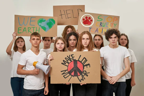 一群激进的高加索青少年拿着硬纸板和平标语参加抗议集会 做爱而不是战争 我们地球 救命啊别再虐待动物了在演播室里被白色背景隔离 — 图库照片