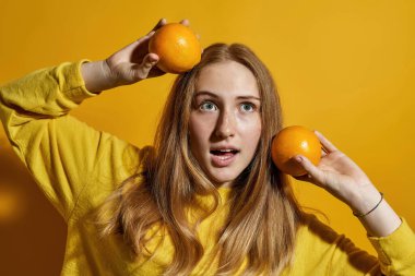 İki portakalla poz veren beyaz bir genç kızın kısmi görüntüsü. Zoomer kuşağının kızı. Sağlıklı beslenme. Modern gençlik yaşam tarzı kavramı. Stüdyoda sarı arka planda izole edilmiş. Boşluğu kopyala