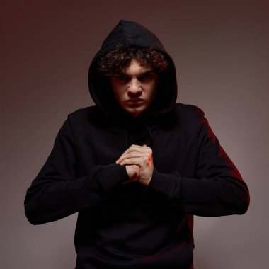 Ciddi bir beyaz çocuk yumruğunu hazırlıyor ve kameraya bakıyor. Zoomer kuşağının kıvırcık adamı. Modern gençlik yaşam tarzı kavramı. Kahverengi üzerine izole edilmiş, beyaz ışıklı arka plan. Stüdyo çekimi