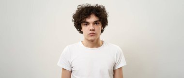 Kameraya bakan beyaz bir gencin portresi. Zoomer neslinin kıvırcık siyah saçlı adamı. Modern gençlik yaşam tarzı kavramı. Beyaz arka planda izole edilmiş. Stüdyo çekimi. Boşluğu kopyala