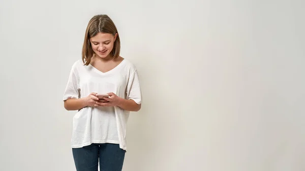 白人の10代の少女がスマートフォンを閲覧 Tシャツとジーンズを着てゾマー世代のブロンドの女性 現代の若いライフスタイルの概念 白い背景に隔離されている スタジオ撮影 スペースのコピー — ストック写真
