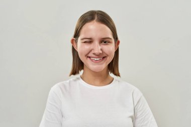 Gülümseyen beyaz ergen kız göz kırpıyor ve kameraya bakıyor. Zoomer kuşağının kadın tişörtü. Modern gençlik yaşam tarzı kavramı. Beyaz arka planda izole edilmiş. Stüdyo çekimi. Boşluğu kopyala