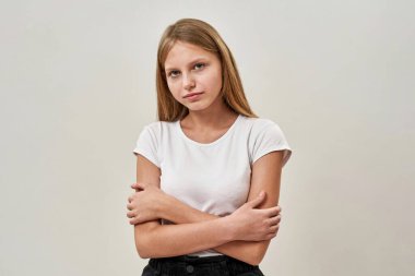 Kollarını kavuşturup kameraya bakan kendine güvenen beyaz kız. Zoomer kuşağının dişi çocuğu. Modern gençlik yaşam tarzı kavramı. Beyaz arka plan. Stüdyo çekimi. Boşluğu kopyala