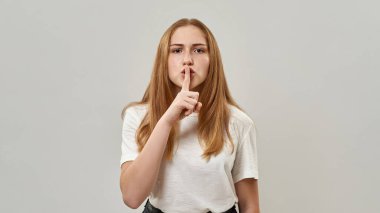 Beyaz kadın ergen sessiz hareketler yapıyor ve kameraya bakıyor. - Gizli. Zoomer kuşağından çilli bir kız. Modern genç yaşam tarzı. Stüdyoda beyaz arka planda izole edilmiş. Boşluğu kopyala
