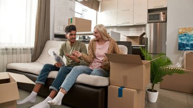 Orta Doğulu bir adam, modern geniş dairedeki koltukta, hava kabarcığı filminde şarap şişesini açmak için beyaz bir kızdan makas alıyor. Çok ırklı genç çift yeni evlerine taşındılar.