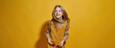 Kameraya bakan gözlüklü, gülümseyen beyaz küçük bir kız. Yakınlaştırma neslinin çocuğu. Modern çocukluk yaşam tarzı kavramı. Sarı arka planda izole edilmiş. Stüdyo çekimi. Boşluğu kopyala