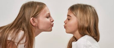 Uzaktan öpüşen genç bir kız ve genç bir kızın kesikli yan görüntüsü. Zoomer kuşağının Avrupalı kız kardeşleri. Gözleri kapalı. Modern genç yaşam tarzı. Beyaz arka planda izole edilmiş. Stüdyo çekimi