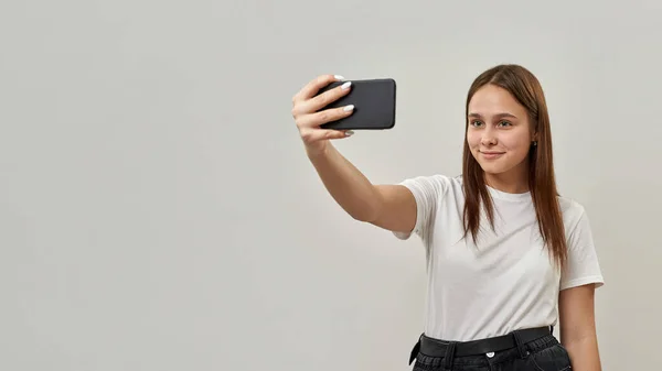 スマートフォンで自撮りする白人女性10代の笑顔 Tシャツとジーンズを着た動物園世代の女の子 現代の若いライフスタイル 白い背景に隔離されている スタジオ撮影 スペースのコピー — ストック写真