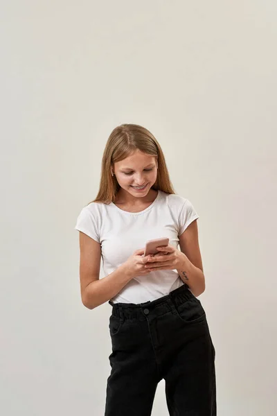 10代の白人の少女がイヤフォンを使い スマートフォンを見ている ゾマー世代のかわいいブロンドの女性の子供 現代の若いライフスタイル スタジオの白い背景に隔離されています スペースのコピー — ストック写真