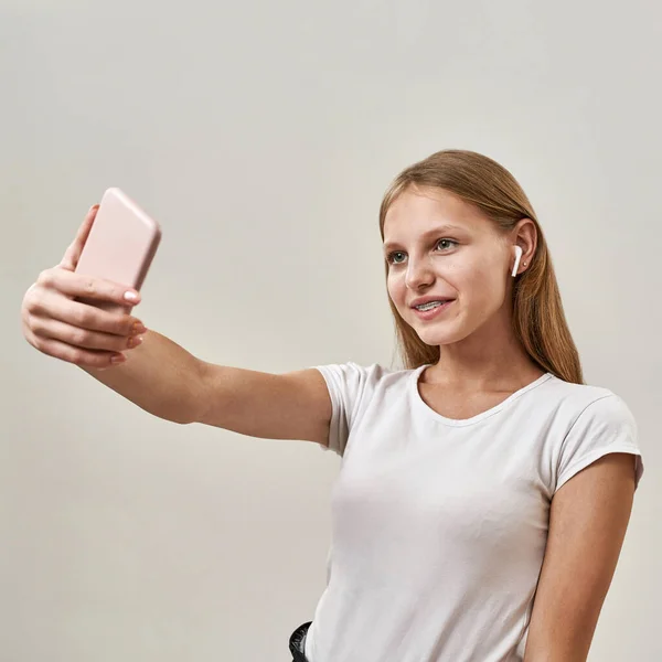 笑顔の白人10代の少女の一部がスマートフォンで自撮りしています ゾマー世代の女性の子供はイヤホンを着用します 現代の若いライフスタイル スタジオの白い背景に隔離されています スペースのコピー — ストック写真