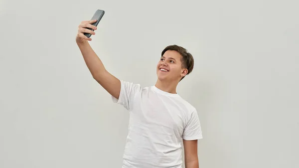 在智能手机上笑高加索少年自私自利 一个穿T恤的男同性恋 现代年轻人生活方式的概念 被白色背景隔离 工作室拍摄 复制空间 — 图库照片