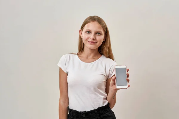 笑顔の白人の10代の少女は 携帯電話を示し カメラを見て ゾマー世代のブロンドの女性の子供 現代の若いライフスタイル 白い背景に隔離されている スタジオ撮影 スペースのコピー — ストック写真