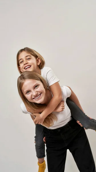 Teenage Girl Holding Little Sister Piggyback Cheerful Caucasian Sisters Zoomer — Stock Photo, Image