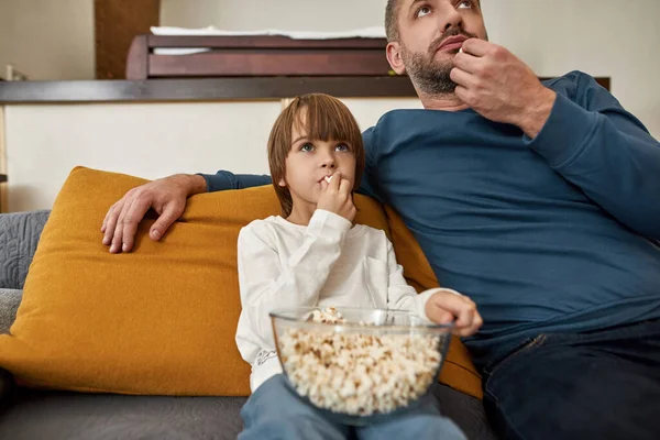 家庭でソファの上でテレビや映画を見て 集中白人の父と息子 ポップコーンを食べる小さな子供 父親と子育て 家族で一緒に過ごす時間 国内レジャー — ストック写真