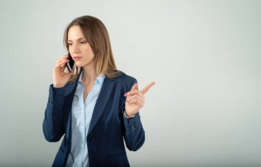 Genç iş kadını, gri arka planda izole edilmiş bir cep telefonuyla konuşuyor.