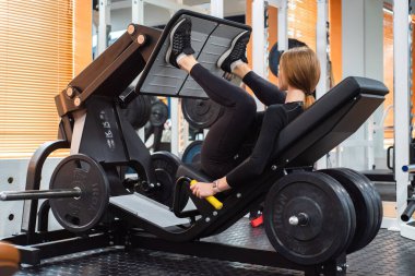 Genç sportif kadın bacak basın makinesi üzerinde bacak egzersizleri yapar