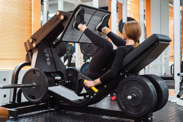 Unga sportig kvinna gör ben övningar på benet press maskin — Stockfoto