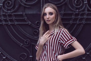 Uzun saçlı genç model metal kapı arkasında poz veriyor.