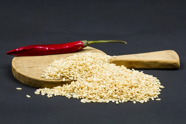 Pimenta vermelha, arroz paddy e tábua de corte de cozinha — Fotografia de Stock