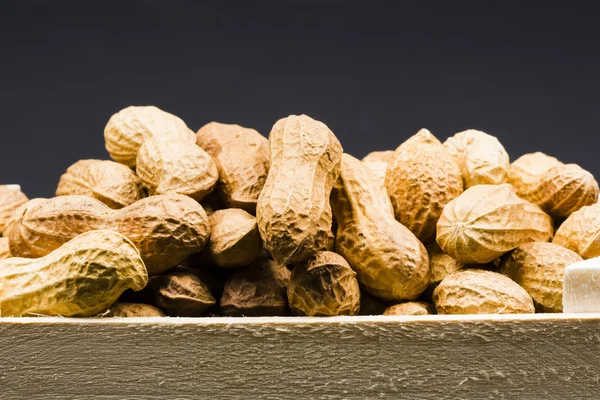 Cacahuetes en cáscara en una caja de madera, con fondo negro — Foto de Stock