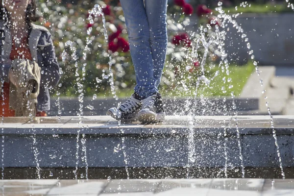 Water drops from a fountain with young girls feet, dressed in jeans