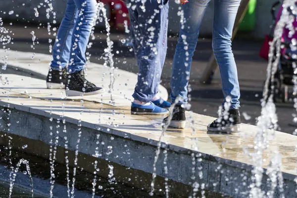 युवा लड़कियों के पैरों के साथ एक फाउंटेन से पानी गिरता है, जीन्स में पहने हुए — स्टॉक फ़ोटो, इमेज