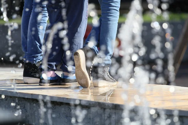 Water drops from a fountain with young girls feet, dressed in jeans — Stock Photo, Image