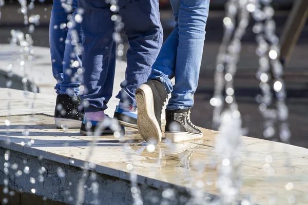 Water drops from a fountain with young girls feet, dressed in jeans — Stock Photo, Image