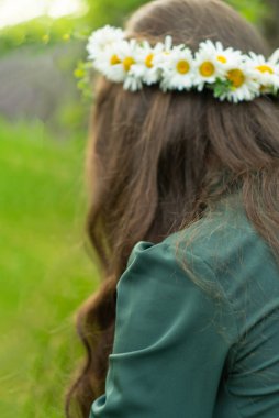 Parkta güzel, kahverengi, uzun saçlı bir kadın yürüyor. Kafasında taze papatya çelengi ve kır çiçekleri var. Saç ürünleri reklamları için bulanık arka plan alanı. Seçici odak