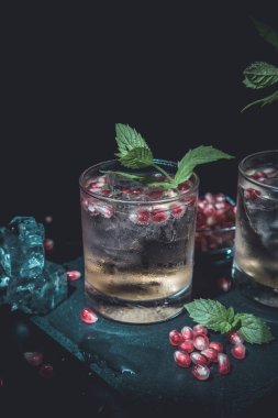 İki karamsar yaz içeceği, siyah arka planda nane, nar ve buz.
