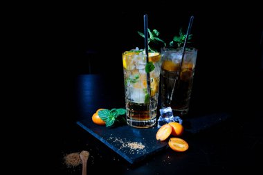 İki renkli yaz içkisi, siyah bir masada nane ve kumkatlı..
