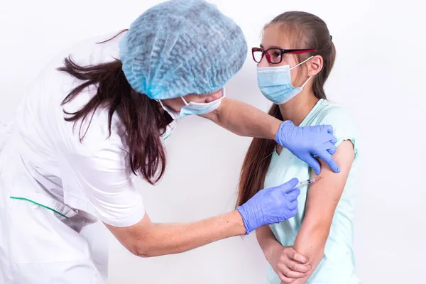 女性小児科医や看護師は、肩の患者にショットやワクチンを与える-若い女の子.インフルエンザ、パンデミックコロナウイルスに対するワクチン。ウイルスからの免疫のための人々の必須予防. ストック写真