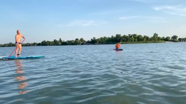 Eine erwachsene glückliche Frau und ein Mann schwimmen auf einem Ruderbrett. Sup-Surfen für Senioren. Sommerunterhaltung und Freizeit, Paddeln im Meer. Ein aktiver Lebensstil. Wassersport. — Stockvideo