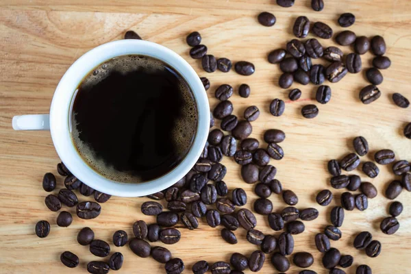 Black coffee is placed on a wooden table with coffee beans.