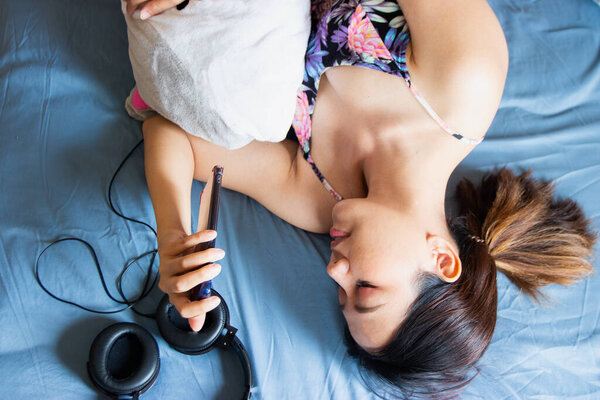 A beautiful Asian woman relaxing and playing smartphone on the bed.