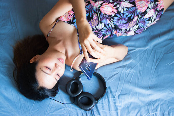 A beautiful Asian woman relaxing and playing smartphone on the bed.