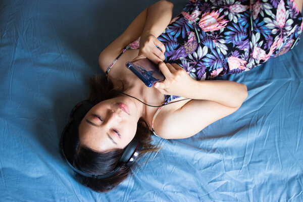 A beautiful Asian woman relaxing and playing smartphone on the bed.