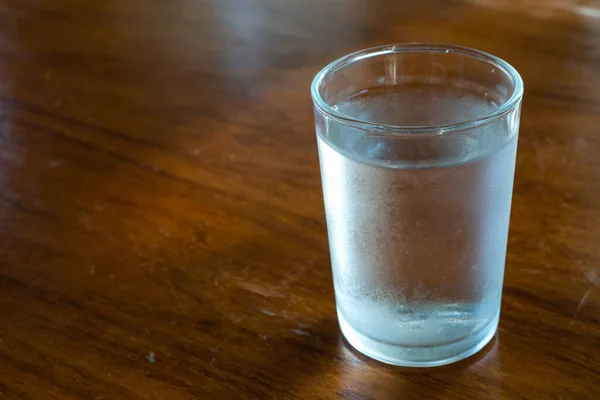 A glass of cool drinking water on a wooden table.