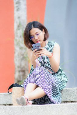 Güzel Asyalı kadın bahçede oturmuş cep telefonuyla oynuyor. Doğayla tatilde dinleniyor..