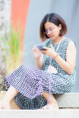 Güzel Asyalı kadın bahçede oturmuş cep telefonuyla oynuyor. Doğayla tatilde dinleniyor..