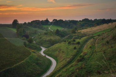 Güzel bir akşam manzarası. Gün batımında yeşil tepeler arasındaki yol.