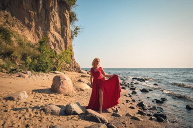 Yaratıcı tatil deniz kenarı seansı. Sahilde zarif kırmızı elbisesiyle güzel bir kadın..